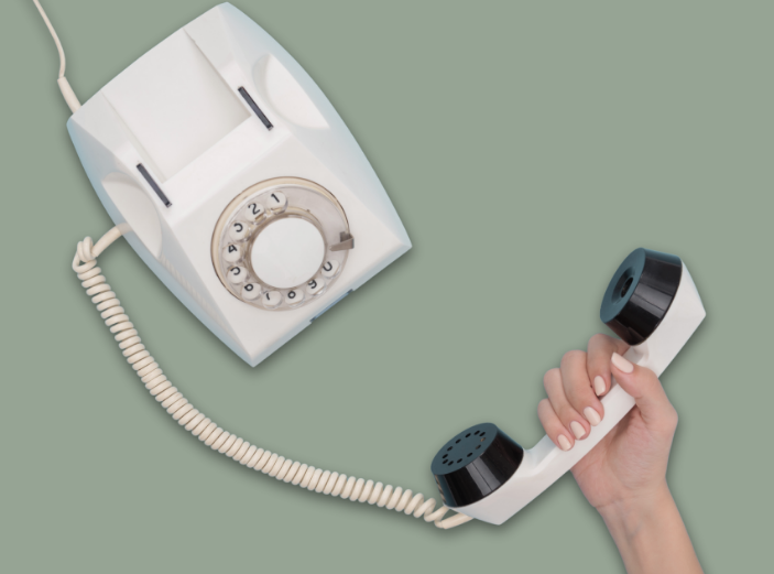 en kvinnlig hand håller i en gammal telefonlur där sladden sedan går upp till en gammal telefon som man hade på 80-talet.