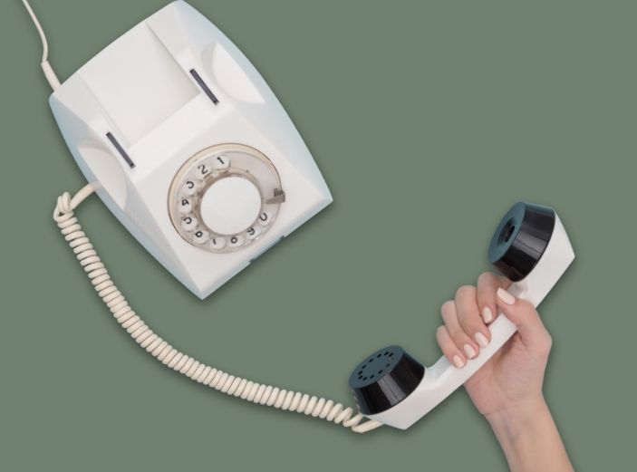en kvinnlig hand håller i en gammal telefonlur där sladden sedan går upp till en gammal telefon som man hade på 80-talet.
