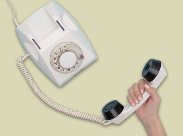 en bild där bakgrunden är ljusgrön och en kvinnlig hand håller i en gammal telefonlur där sladden sedan går upp till en gammal telefon som man hade på 80-talet.