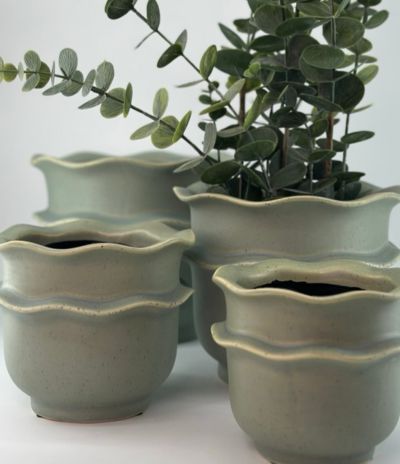 En bild på en vas som står på ett cafébord utomhus. Det är en stol bredvid i samma serie som bordet i en turkos färg. I den blåa vasen på bordet är det visa rosenskära-blommor i. Här kommer du vidare till krukor & vaser.